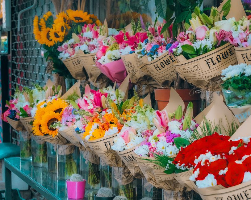 A display of vibrant fresh flower bouquets arranged on a glass counter at a floral shop, featuring a variety of blooms including bright yellow sunflowers, pink and white lilies, multicolored carnation