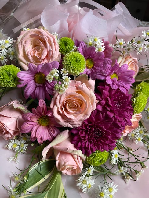 A vibrant bouquet of fresh flowers featuring soft pink roses with tightly curled petals, bright purple daisies with yellow centers, and small white daisies with yellow centers and delicate petals. Int